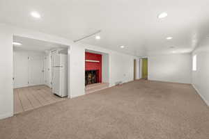 Basement featuring light colored carpet, freestanding refrigerator, a warm lit fireplace, and recessed lighting
