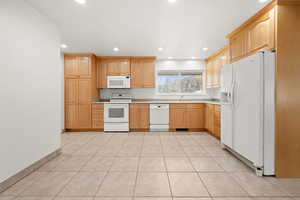 Kitchen with white appliances, light wood finish cabinets, light countertops, recessed lighting, and light tile patterned flooring