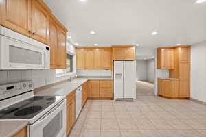 Kitchen featuring white appliances, light countertops, light wood finish cabinets, tasteful backsplash, and recessed lighting