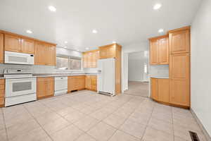 Kitchen with light wood finish cabinetry, white appliances, backsplash, light tile patterned flooring, and recessed lighting