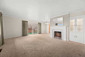 Unfurnished living room featuring crown molding, a fireplace, carpet floors, and a chandelier
