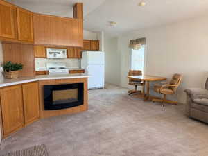 Kitchen featuring wood finish cabinets, white appliances, light countertops, open floor plan, and vaulted ceiling