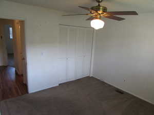 Unfurnished bedroom featuring dark carpet, ceiling fan, and a closet