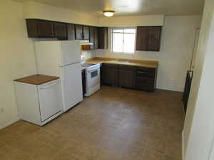 Kitchen featuring white appliances, dark wood finish cabinets, light countertops, and dark flooring