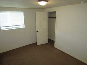 Unfurnished bedroom with dark carpet, a closet, and a textured ceiling