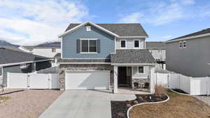 View of front facade featuring a gate, stone siding, a shingled roof, driveway, and an attached garage