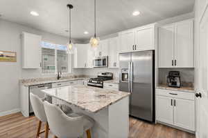 Kitchen featuring stainless steel appliances, light stone countertops, a kitchen island, white cabinets, and light wood-style floors