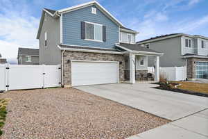 View of front of home with a gate, a garage, driveway, stone siding, and covered porch