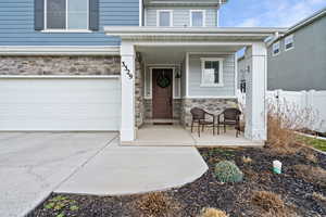 View of exterior entry with stone siding, a porch, an attached garage, and driveway