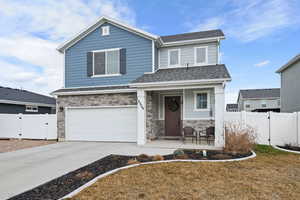 View of front of house featuring a gate, an attached garage, stone siding, and covered porch