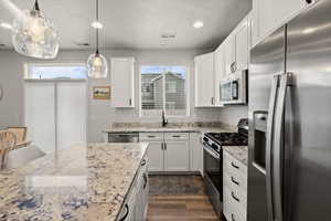 Kitchen with stainless steel appliances, light stone counters, pendant lighting, and white cabinets