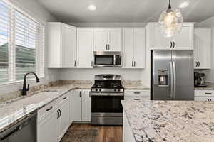 Kitchen featuring stainless steel appliances, white cabinetry, light stone counters, and dark wood finished floors