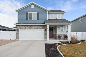 View of front of home with a gate, stone siding, a garage, and covered porch