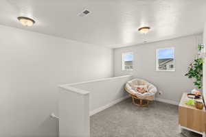 Living area with light colored carpet, a textured ceiling, and an upstairs landing