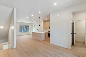 Kitchen with light wood finish cabinets, a center island with sink, open floor plan, hanging light fixtures, and light wood-type flooring