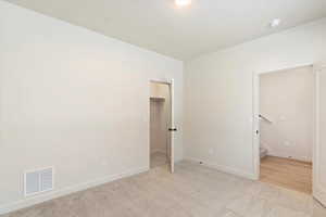 Unfurnished bedroom with a walk in closet and light colored carpet