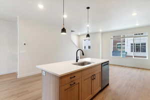 Kitchen featuring pendant lighting, light wood-style floors, an island with sink, dishwasher, and light wood finish cabinetry
