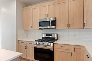 Kitchen with light wood finish cabinetry, stainless steel appliances, and backsplash