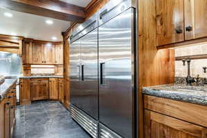 Kitchen featuring backsplash, built in fridge, wood finish cabinetry, dark stone counters, and recessed lighting