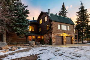 Log home featuring log exterior, a garage, stone siding, and roof with shingles