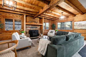 Living room with log walls, a wood ceiling with exposed beams, and a stone fireplace