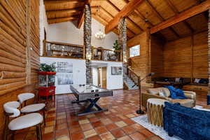 Living room featuring a chandelier, a high wood beamed ceiling, rustic walls, and tile patterned flooring