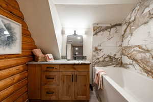 Bathroom with vanity, rustic walls, and a bath