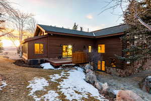Snow covered house with a wooden deck, roof with shingles, and log exterior
