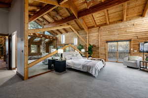 Bedroom with a high wooden beamed ceiling, rustic walls, carpet floors, and access to outside