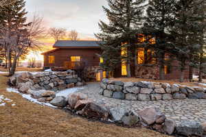 Back of house at dusk featuring log veneer siding and stone siding
