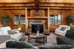 Carpeted living area featuring log walls, a fireplace, and a wooden ceiling with exposed beams