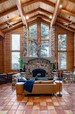 Living room featuring a ceiling fan, a high wooden beamed ceiling, a stone fireplace, tile patterned flooring, and log walls