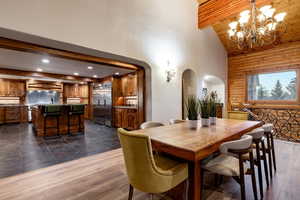Dining space with arched walkways, dark wood finished floors, suspended lighting, and a high wood beamed ceiling