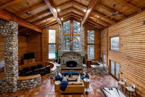 Living area with a ceiling fan, a high wood beamed ceiling, a fireplace, healthy amount of natural light, and log walls
