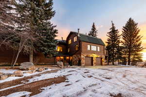 Log cabin featuring stone siding, an attached garage, log exterior, a shingled roof, and a gambrel roof