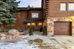 View of front of home with a garage, log exterior, concrete driveway, and stone siding
