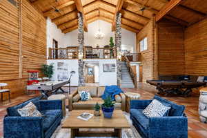Living room featuring rustic walls, a high wood beamed ceiling, suspended lighting, tile patterned floors, and billiards table