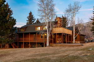 Back of property with a chimney, a lawn, a deck, and a patio