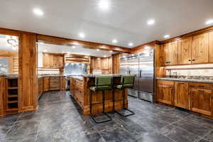 Kitchen featuring tasteful backsplash, a kitchen breakfast bar, a kitchen island, built in fridge, and light stone counters