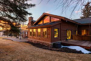 Back of property at dusk featuring a chimney, a yard, and a wooden deck