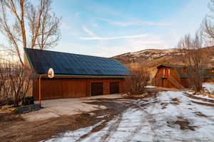 Snow covered garage featuring solar panels, a mountain view, and driveway