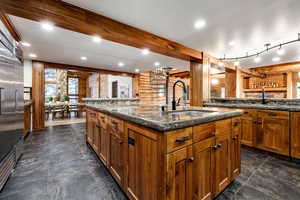 Kitchen featuring rustic walls, dark stone counters, wood finish cabinets, recessed lighting, and built in fridge