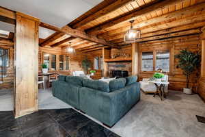 Living area featuring a stone fireplace, log walls, a wooden ceiling with exposed beams, and carpet floors
