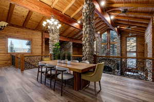 Dining area with log walls, hardwood / wood-style flooring, a chandelier, and a high wooden beamed ceiling