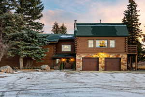 Cabin featuring log exterior, an attached garage, stone siding, and roof with shingles