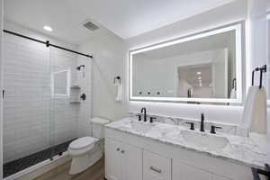 Bathroom with double vanity, a shower stall, recessed lighting, and dark wood finished floors