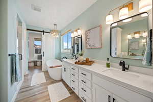 Full bath with double vanity, a soaking tub, light wood-style floors, and a shower stall