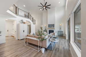 Living area featuring a high ceiling, light wood-type flooring, ceiling fan, a fireplace, and recessed lighting