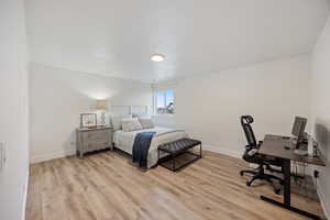 Bedroom with a desk, light wood-style floors, and a textured ceiling