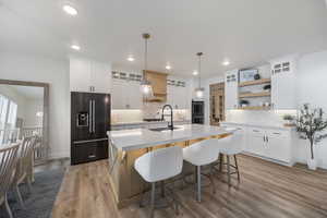 Kitchen featuring glass fronted cabinets, high quality fridge, decorative light fixtures, a center island with sink, and open shelves